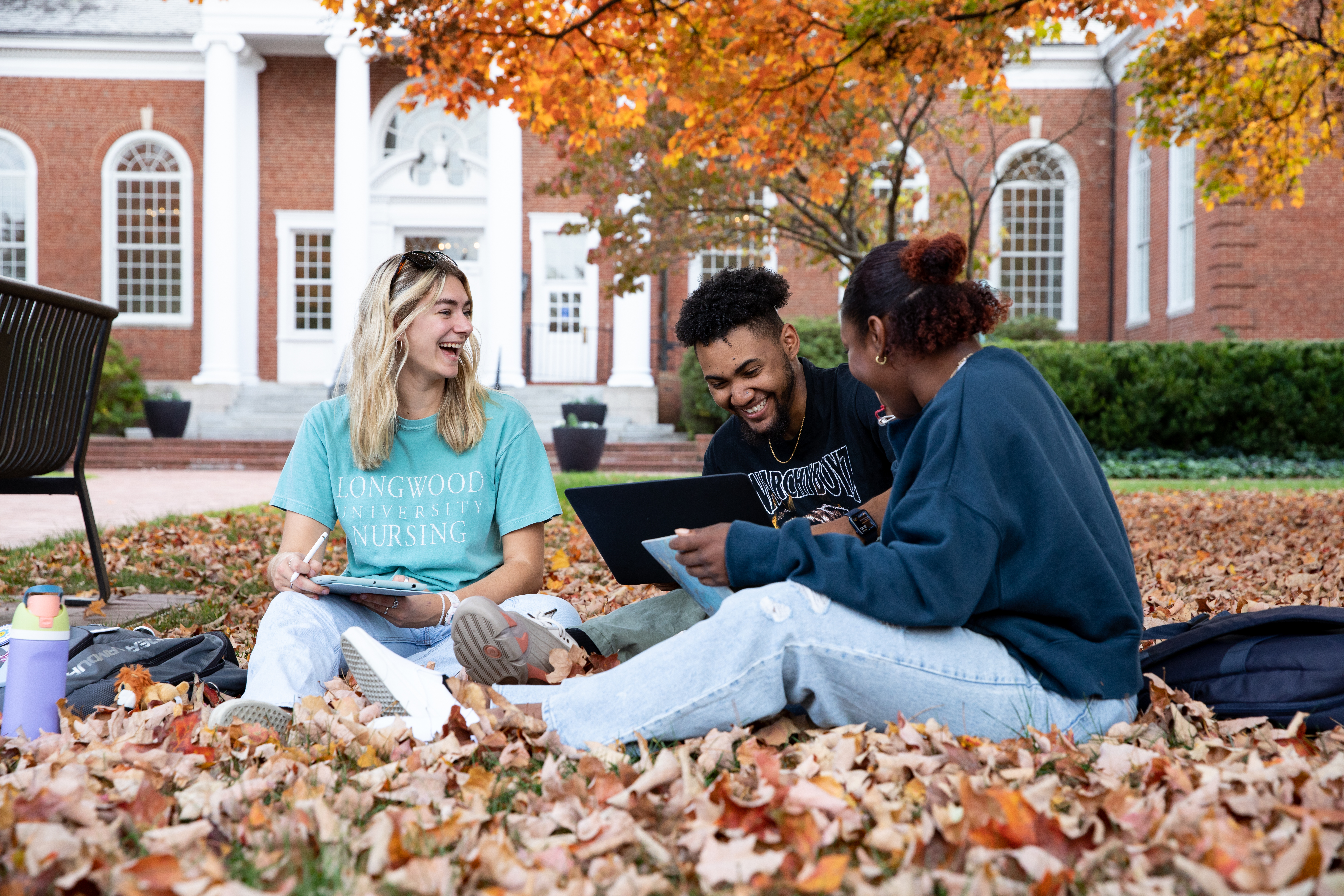Three students sit on the leaf-covered lawn in front of Eason Hall