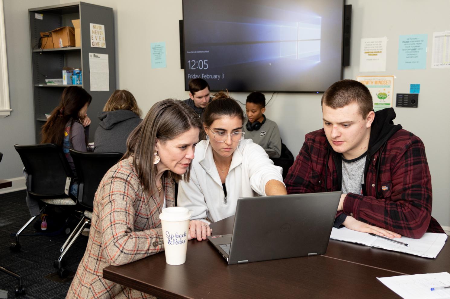 Students and a faculty member work together around a laptop in the Quantitative Reasoning Center, with other students collaborating in the background.